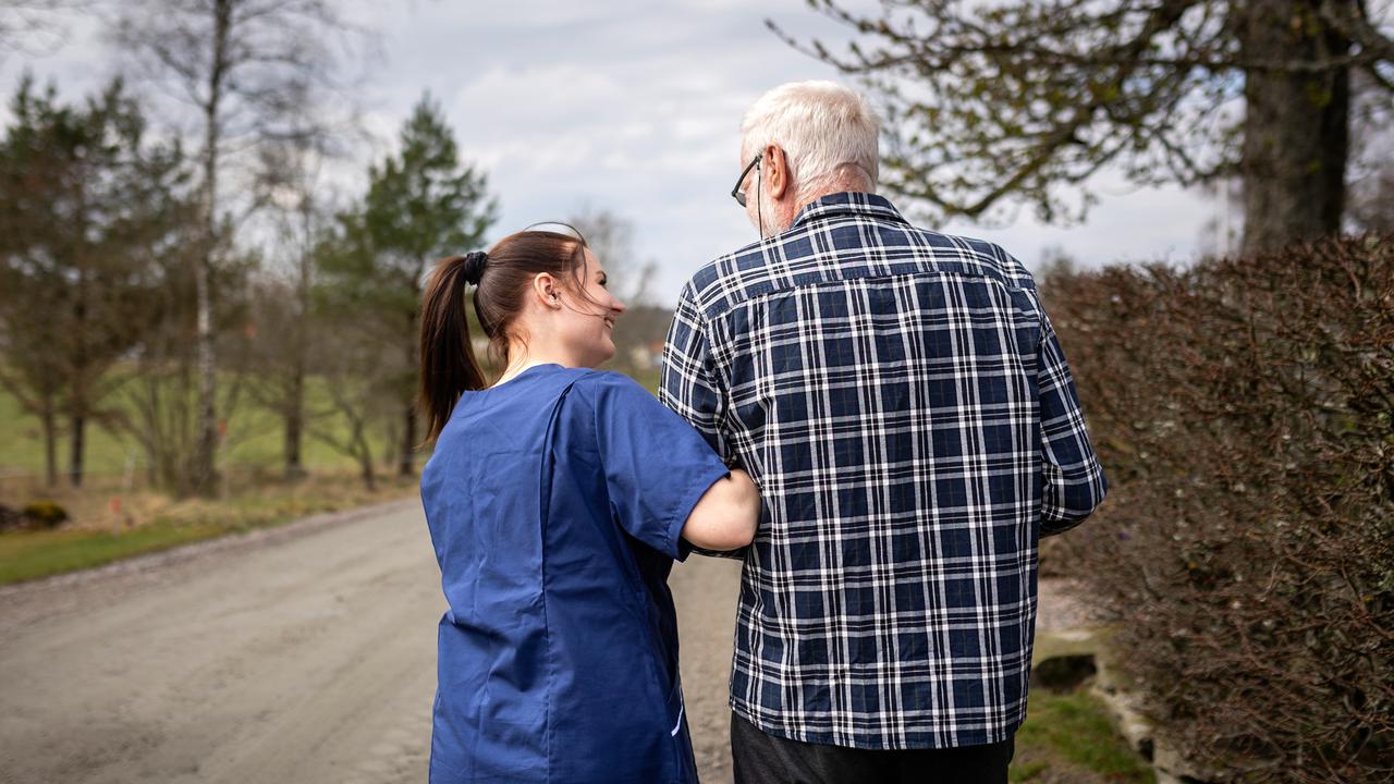 Äldre man får stöd av hemtjänstersonal på grusväg