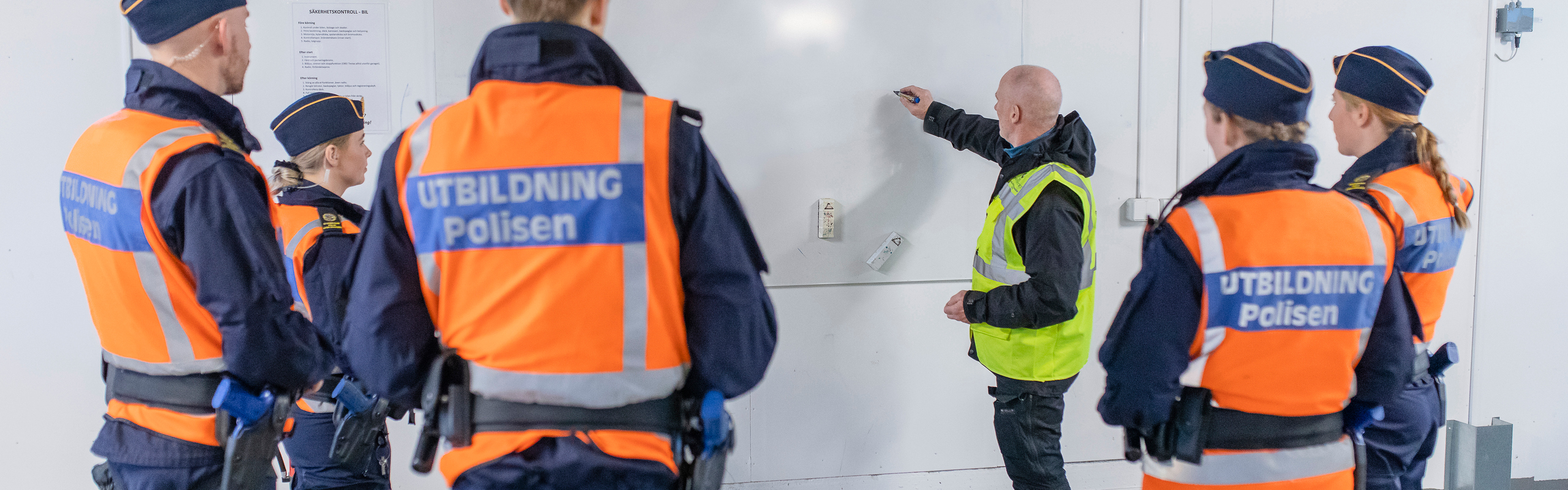 Polislärare Conny Tärnklev instruerar polisstudenter vid vita tavlan i Polisutbildningshusets garage.