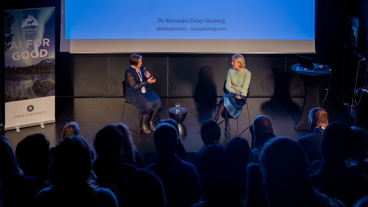 two people talking in frons of audience in dark room