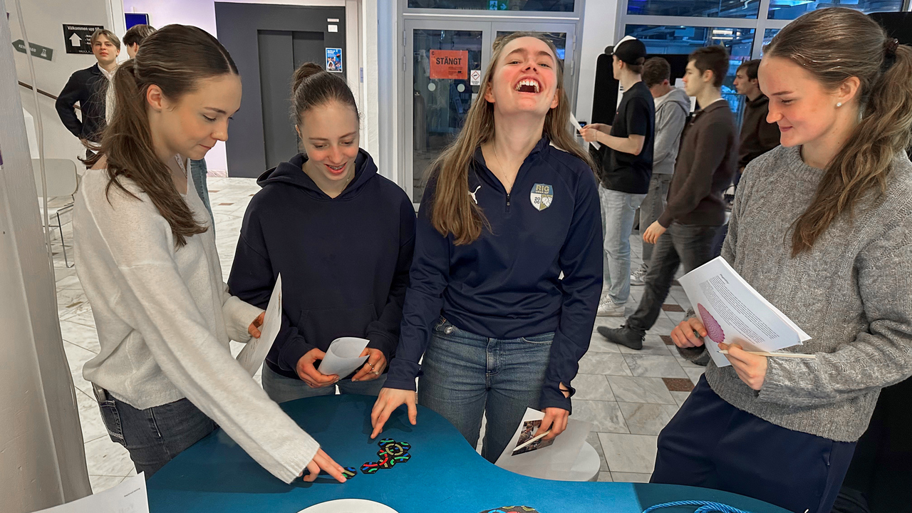 Fyra unga kvinnor deltar i semifinalen av Unga forskare, som arrangerades i Umeå den 28 februari. De står runt ett blått bord och interagerar med färgglada knutar, rep och informationsblad.