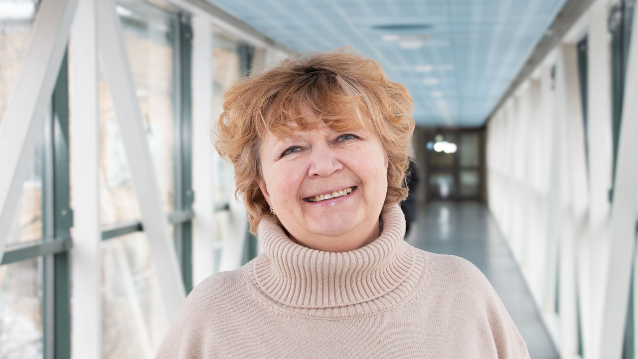 Professor Nina Khairova i en ljus korridor, iklädd en beige tröja. Hennes hår är blont och kort och hon ler.