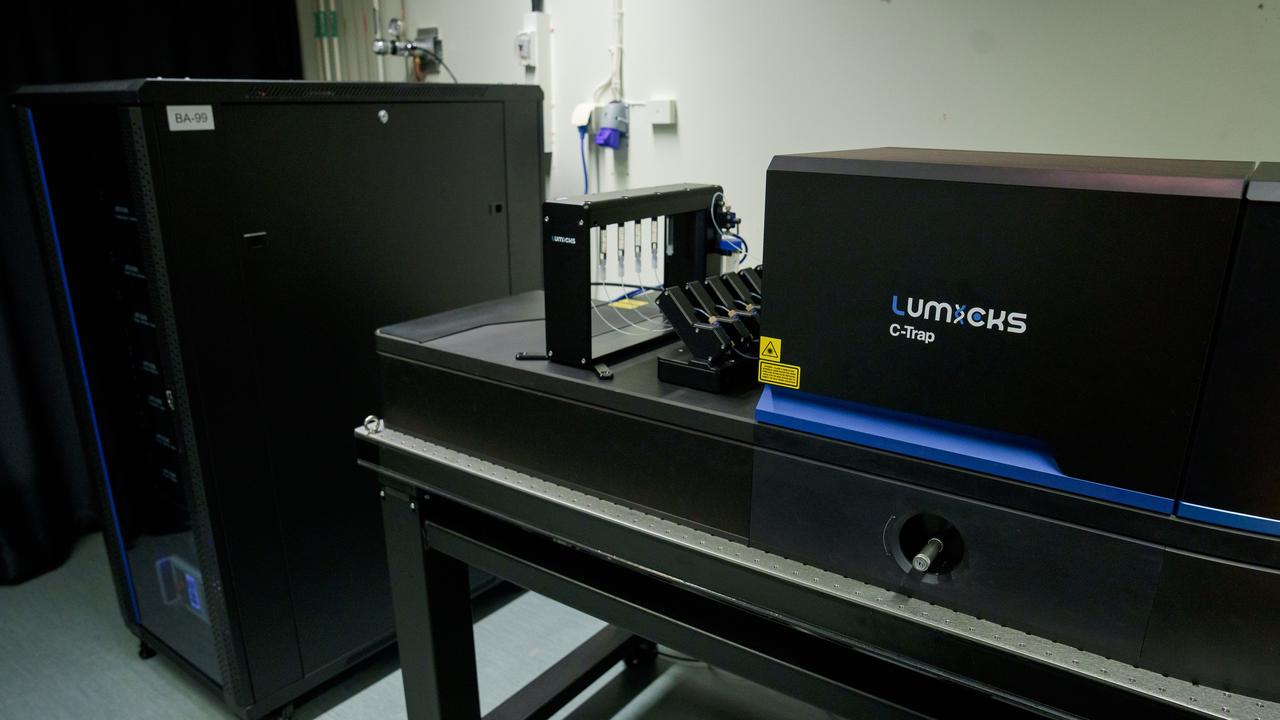 En svart hög låda står längst bak och ett svart bord med ett stativ med kapillärer och en annan svart låda framför, på vilken det står ”Lumicks C-Trap”.