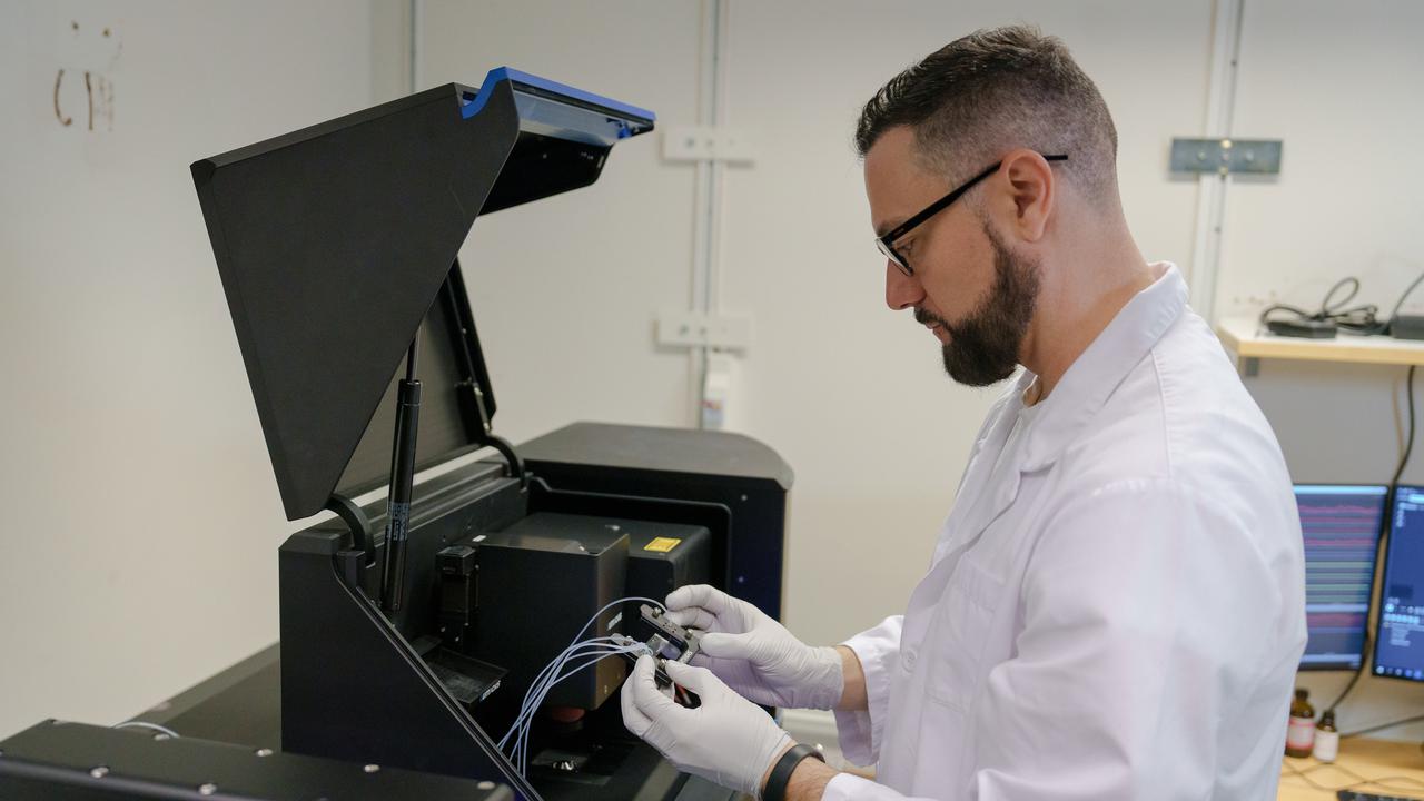 Rubén Casanova Sáez, klädd i vit labbrock och handskar, håller en liten apparat i händerna som är ansluten till små rör.