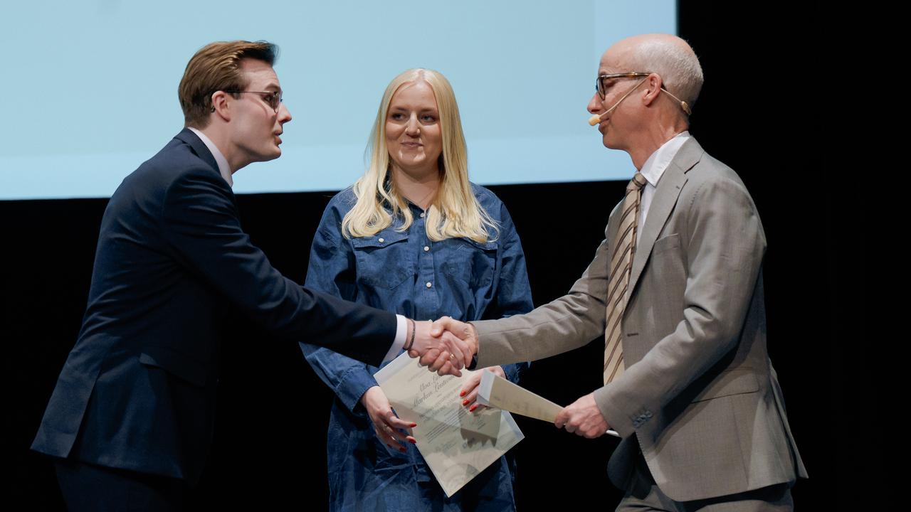 Två män och en kvinna skakar hand på scen.