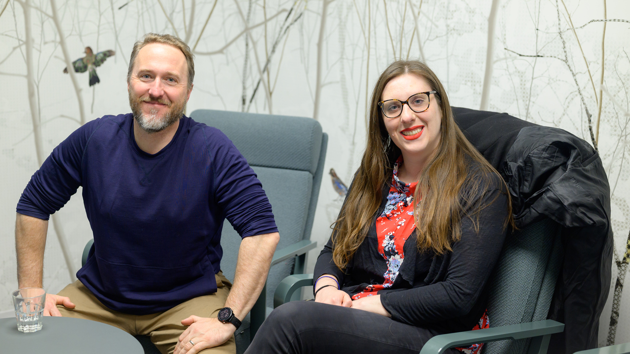 Eric Libby and Laura Carroll sit in IceLab against a background wallpaper of birds
