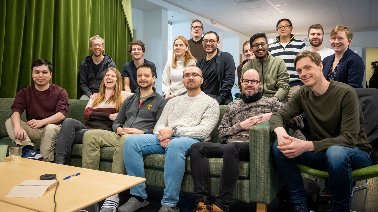 Gruppbild på ett 15-tal glada personer inomhus.