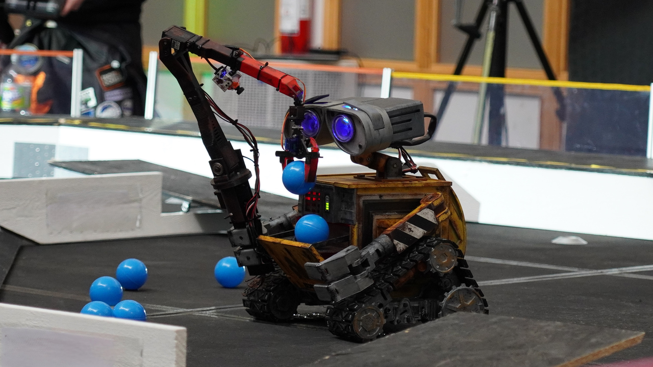 Bild på robot på hjul som plockar upp blå bollar under robottävling.