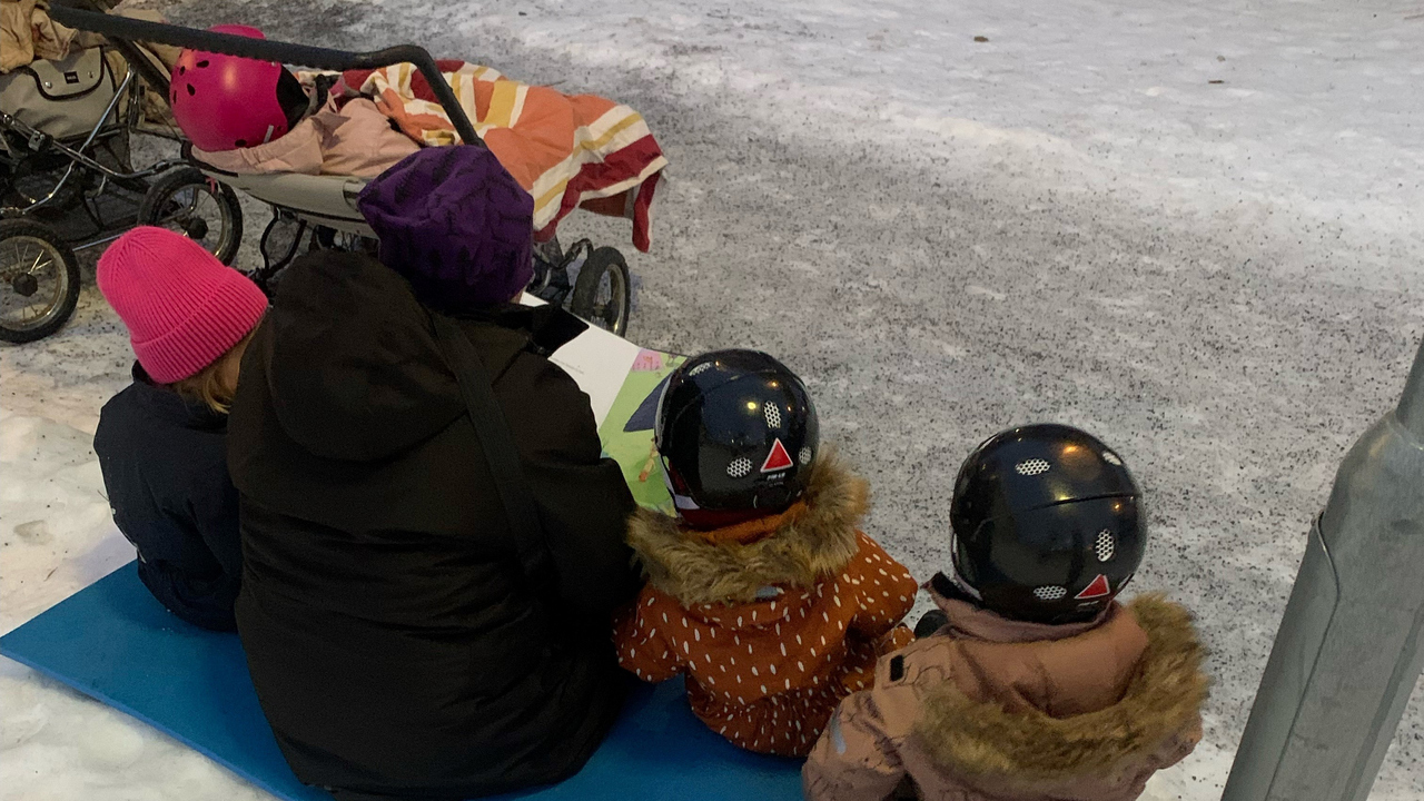 Förskollärare läser bok för barn utomhus på vintern.