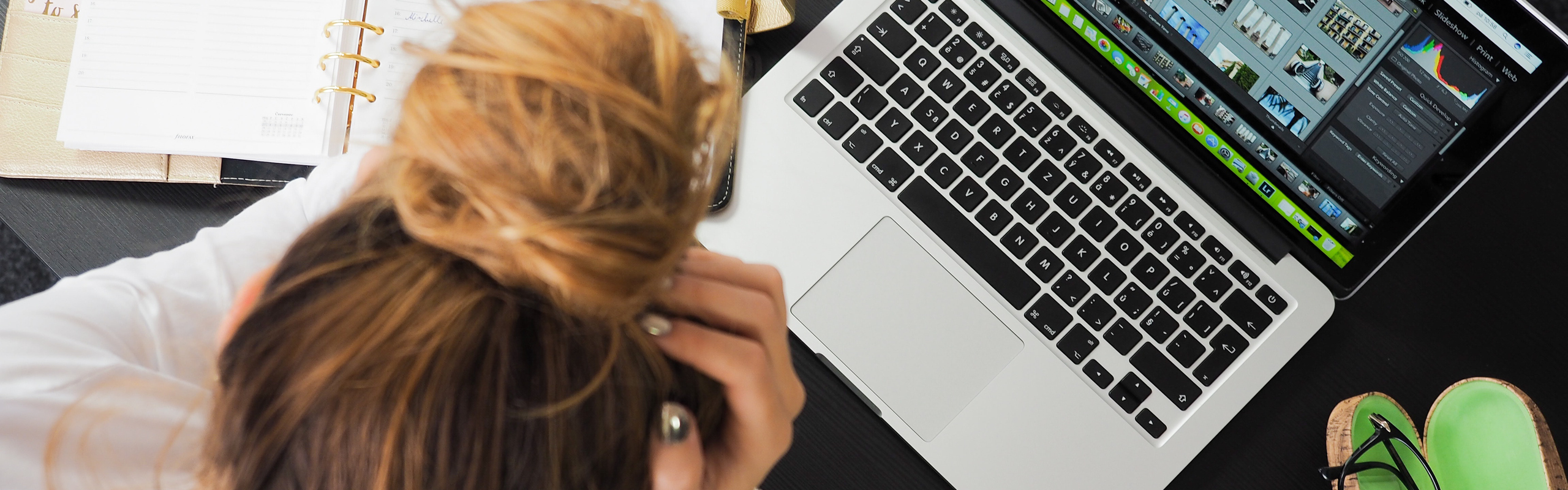 Kvinna sitter med huvudet i händerna vid skrivbord med dator