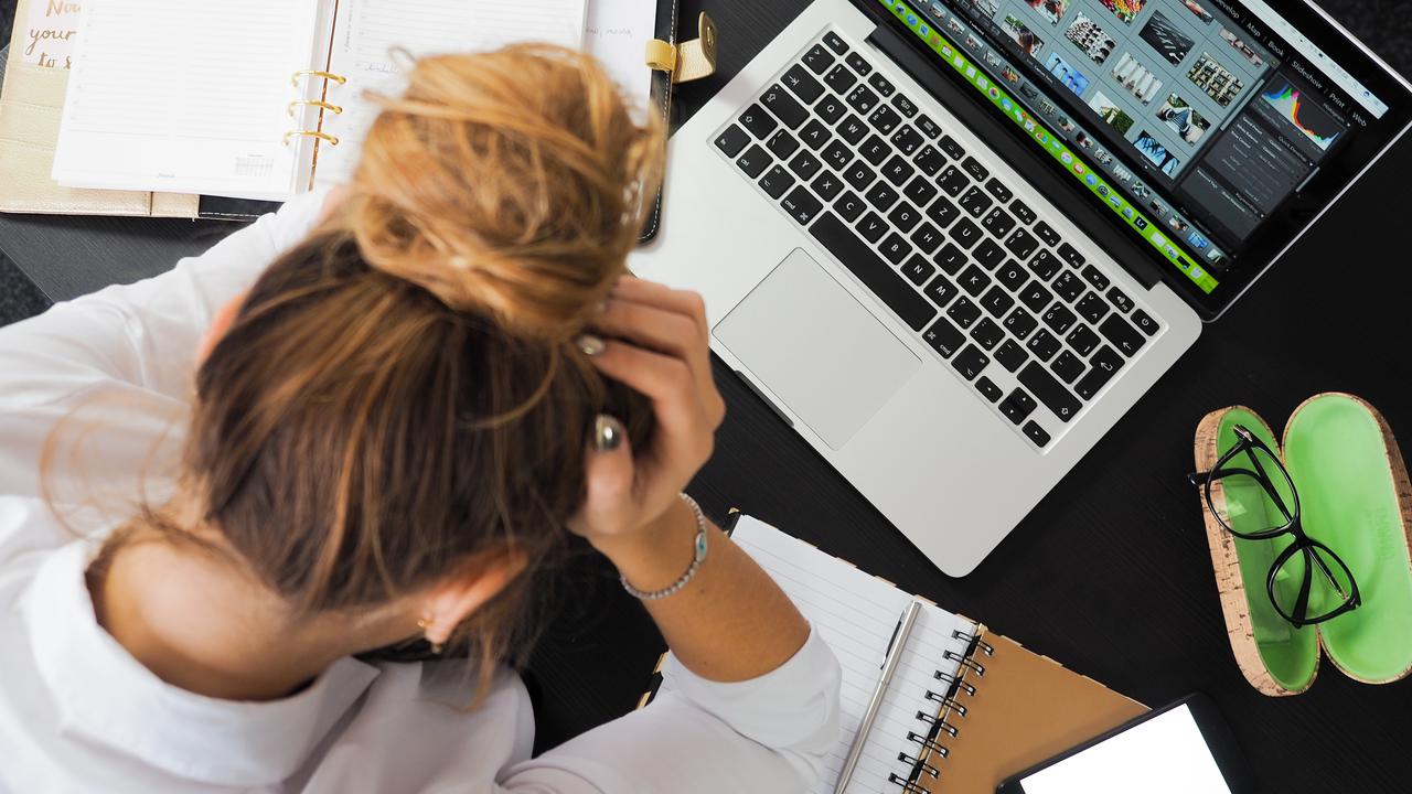 Kvinna sitter med huvudet i händerna vid skrivbord med dator