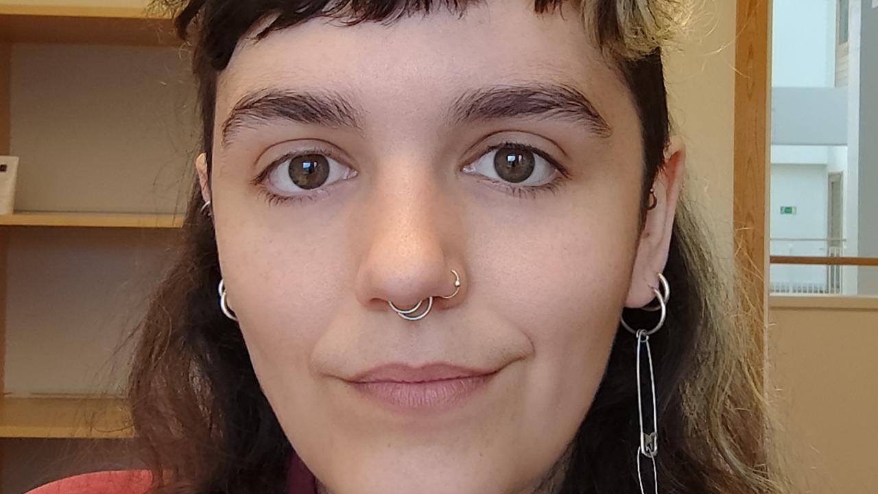 Kvinna med mörkt långt hår, kort lugg och röd skjorta. 