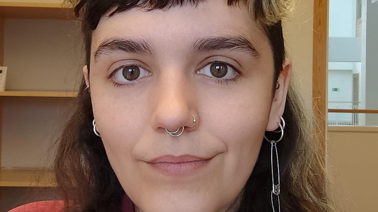 Kvinna med mörkt långt hår, kort lugg och röd skjorta.