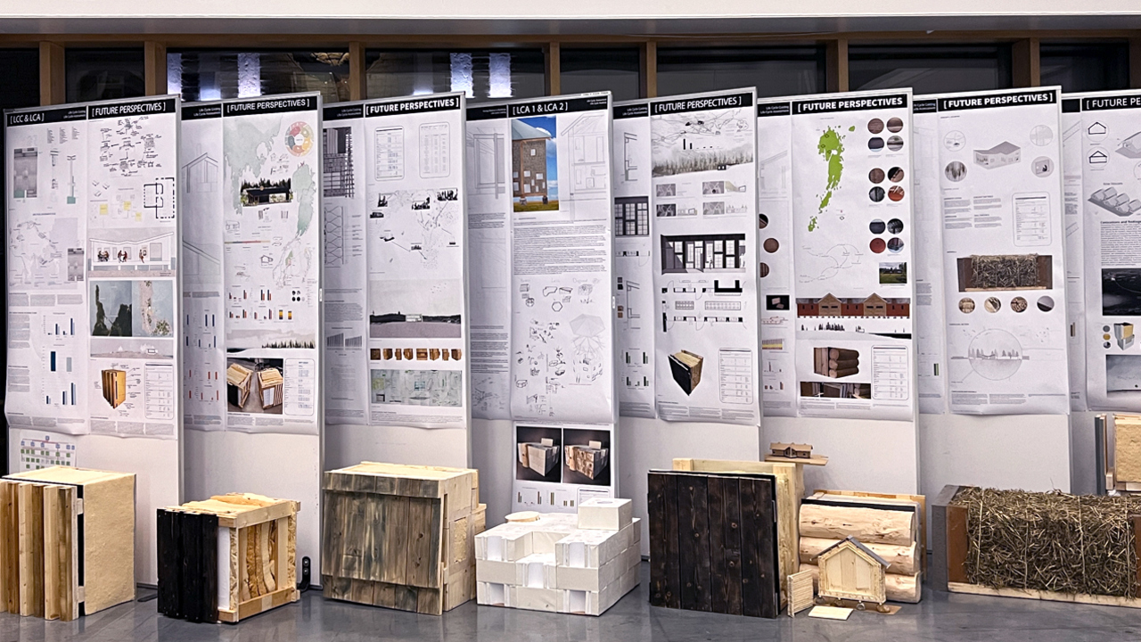 Exhibition in Umeå School of Architecture's entrance with built objects and posters, dark outside