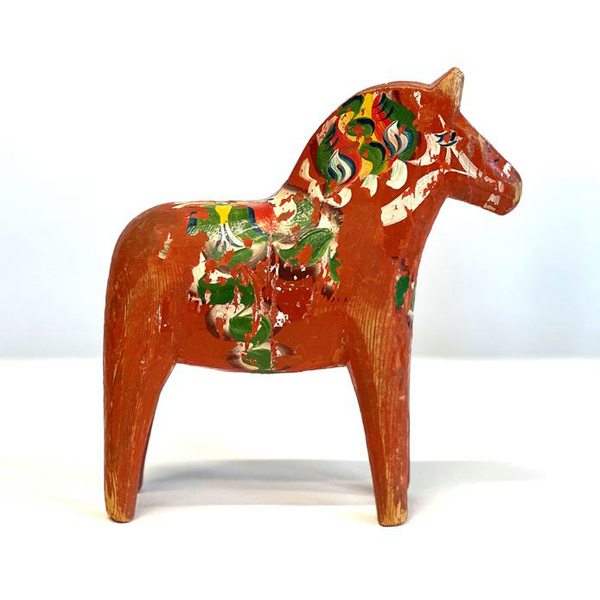 En gammal, röd dalahäst med målat mönster i grönt, vitt och gult.