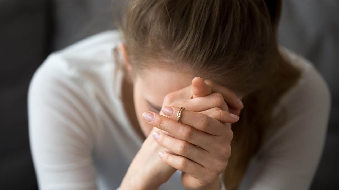 Kvinna som inte mår bra sitter lutad framåt med händerna knäppta framför ansiktet.