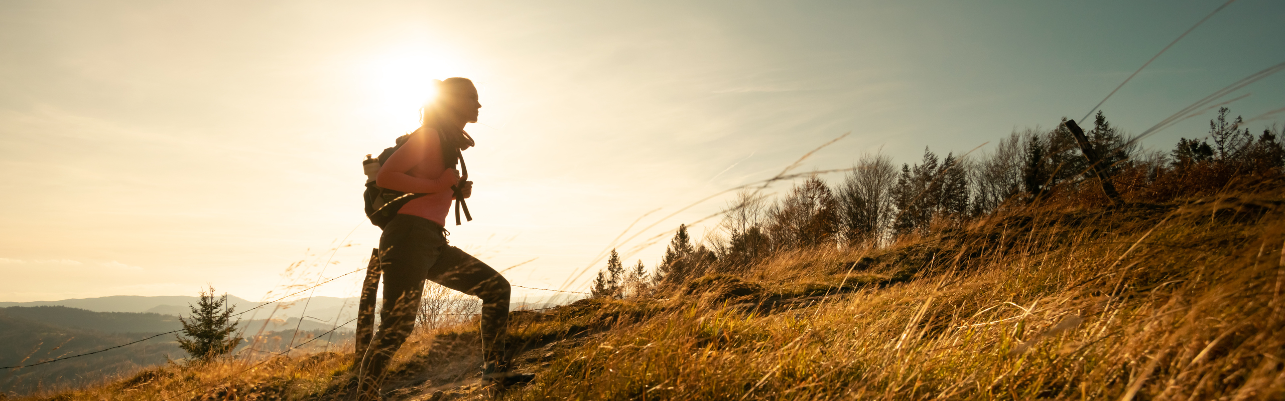 Kvinna vandrar uppför backe i motljus.