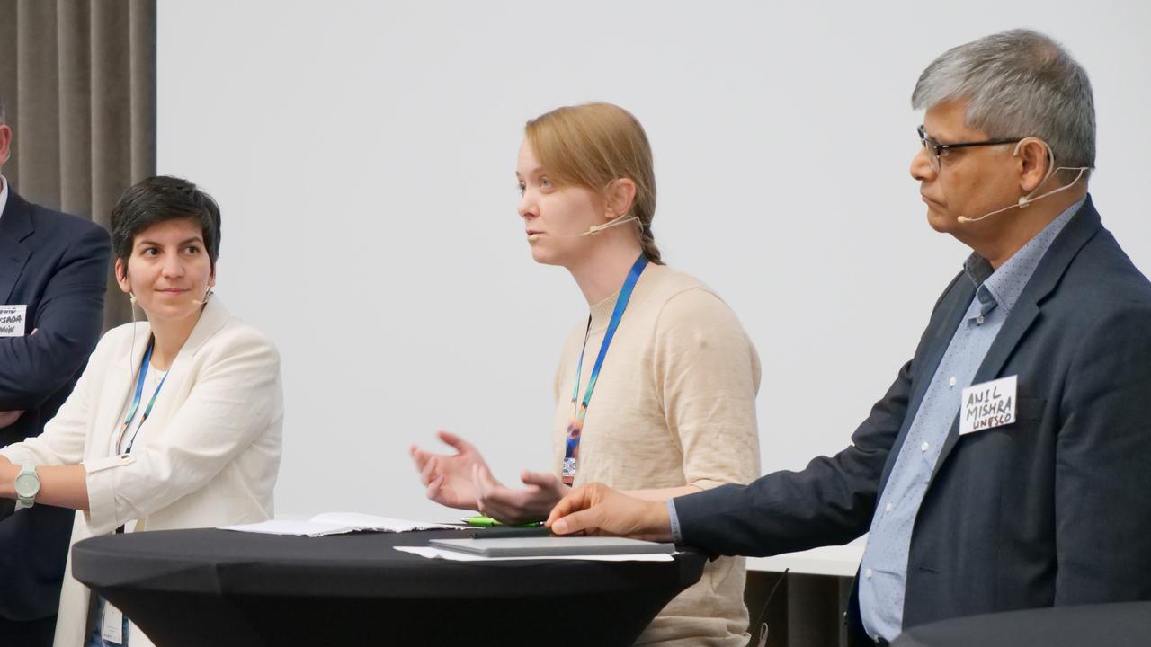 Tre personer står vid ett ståbord och pratar till en publik.