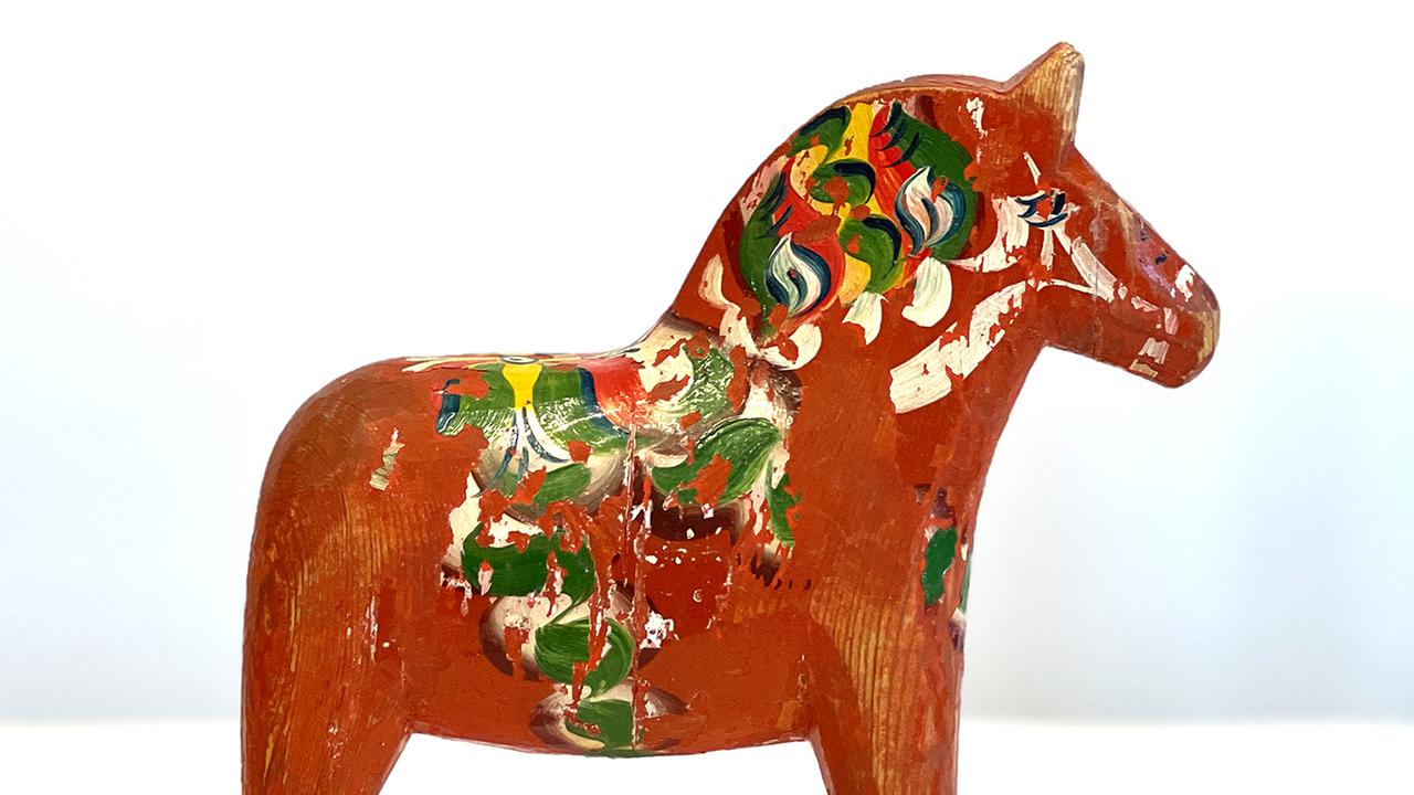 En gammal, röd dalahäst med målat mönster i grönt, vitt och gult.