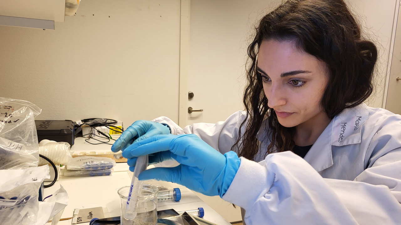 En ung kvinna med vit labrock och blå plasthandskar på sig väger prover på en våg.