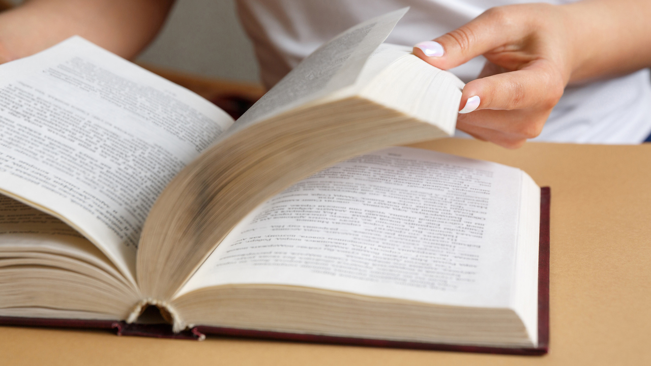 Närbild på händer som bläddrar i en bok.