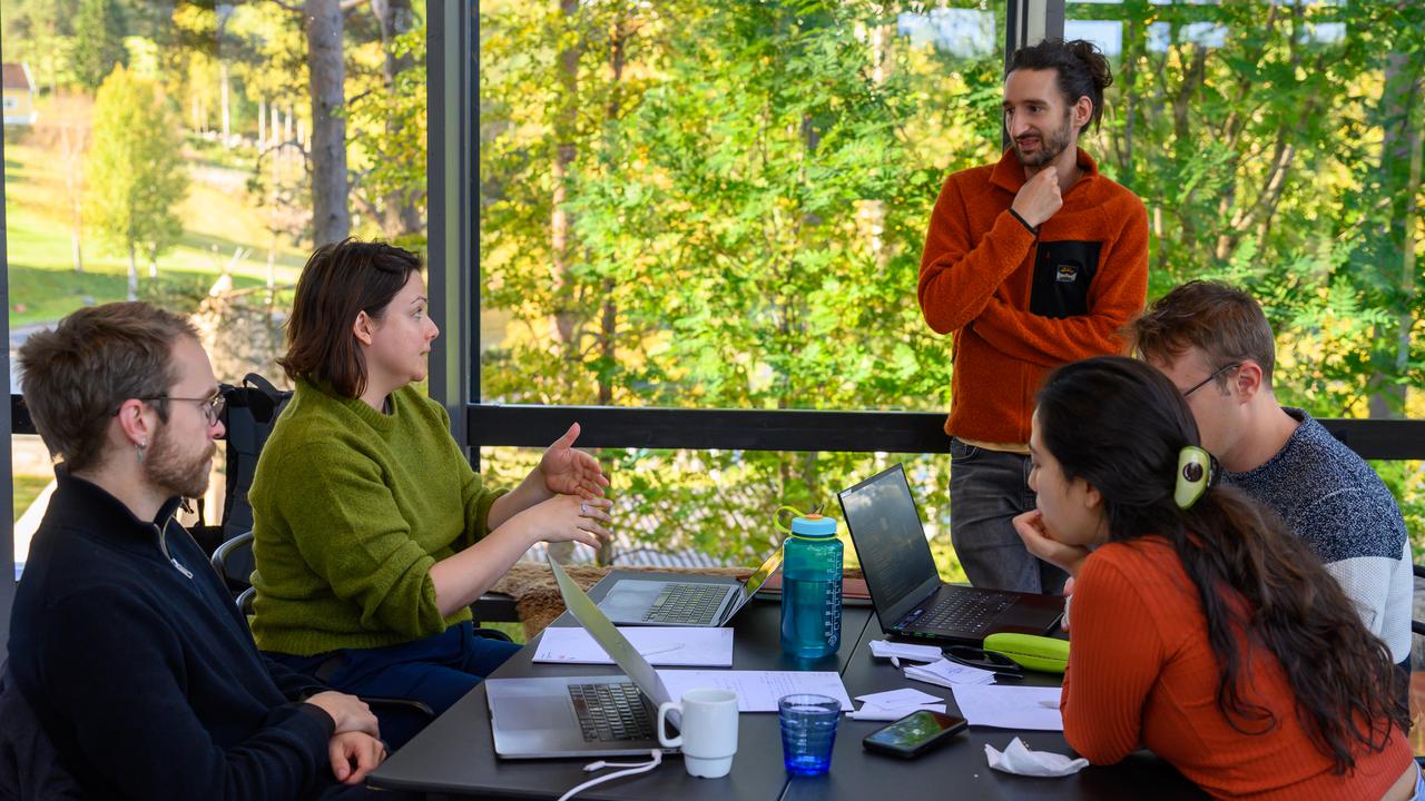 Four people seated look up towards a standing man and converse together