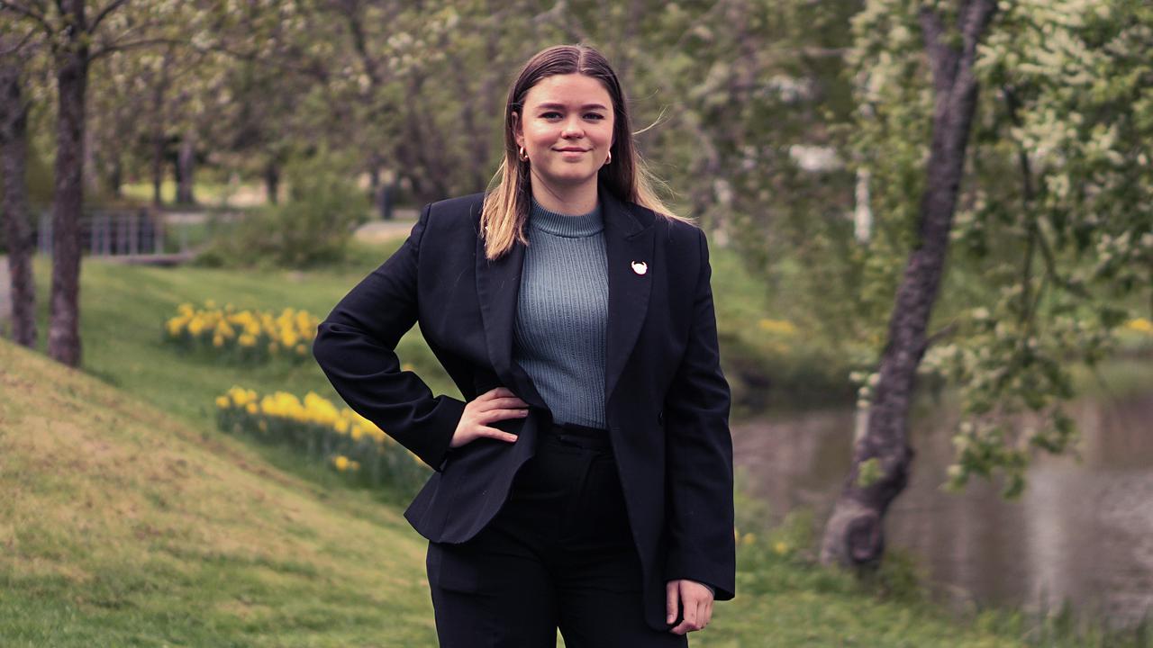 A woman in a black suit stands in front of a river.