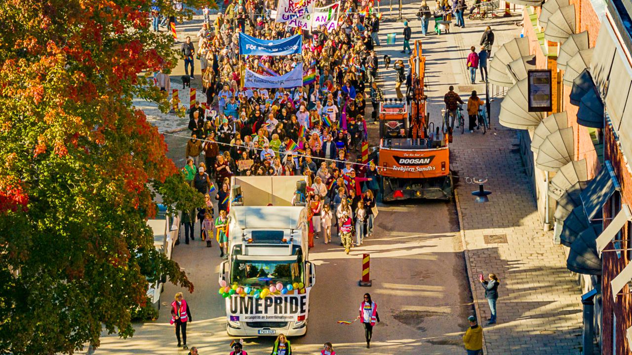 Drone image of a parade of people marching in the Pride parade in Umeå 2024, with rainbow flags and banners. 