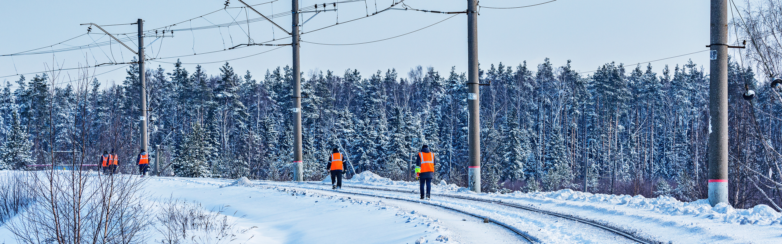 Banarbetare går på räls i vinterlandskap.