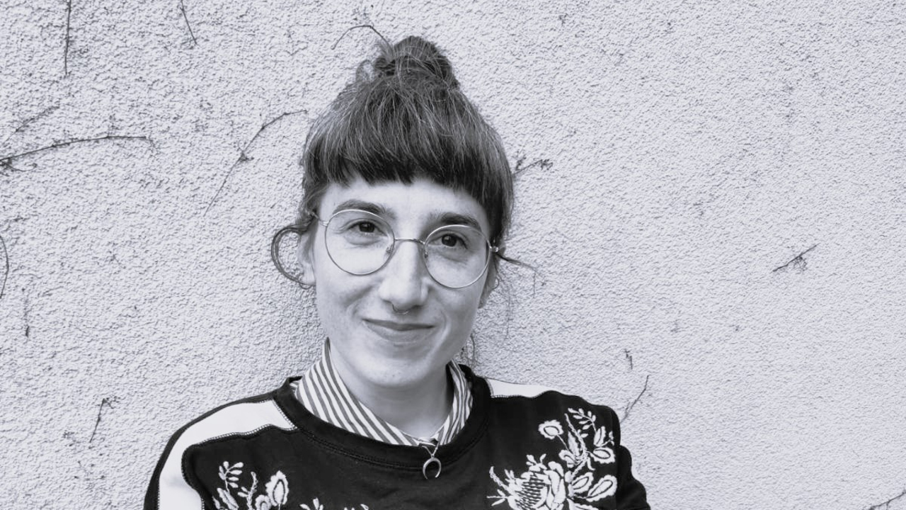 Kvinna som är gästforskare vid Umeå universitet sitter lutat mot en betongvägg. Bilden är svartvit.