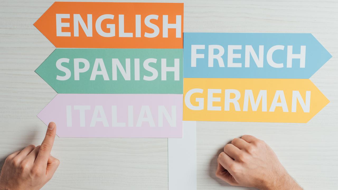 Skyltar med olika språk på som pekar åt olika håll som en hand pekar på. För att illustrera språkinlärning eller livslångt lärande.