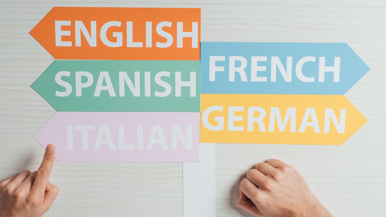 Skyltar med olika språk på som pekar åt olika håll som en hand pekar på. För att illustrera språkinlärning eller livslångt lärande.
