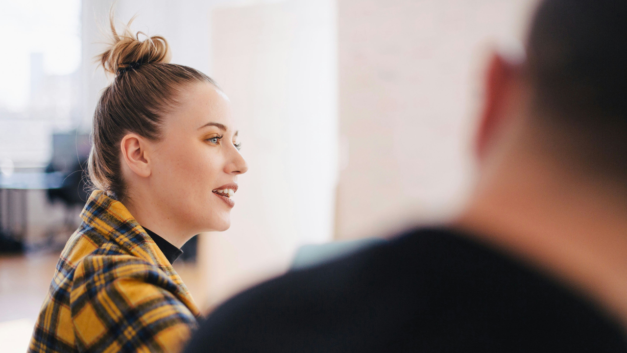 Kvinna i gulrutig kostym talar.