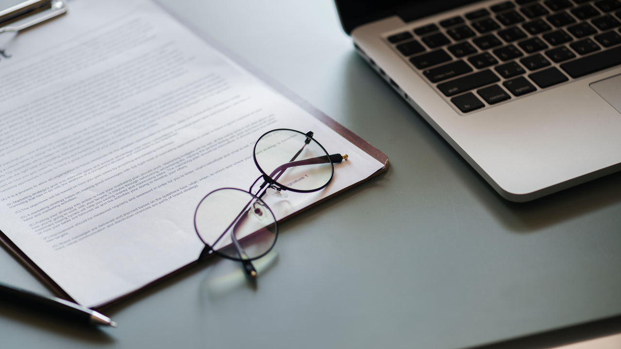 Glasögon liggande på dokument bredvid dator