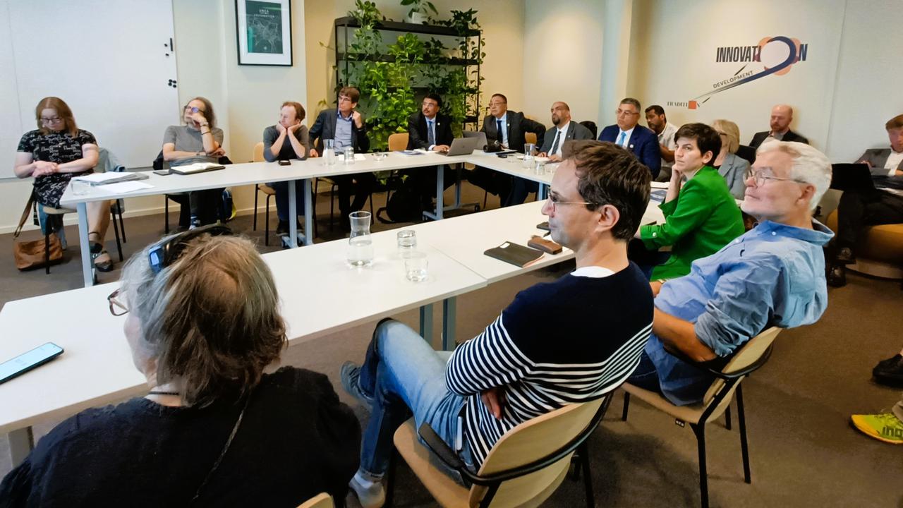 Människor sitter runt ett bord och lyssnar på en presentation.