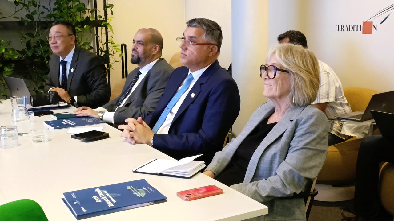 Fyra personer i kostym sitter vid ett bord och lyssnar på en presentation. På bordet ligger forskningsartiklar, anteckningsböcker och glas med vatten i.