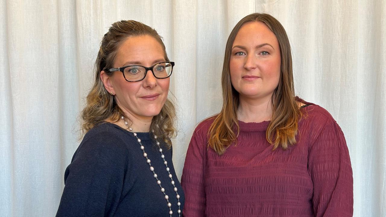 Två kvinnor står framför ett beige draperi. Den ena har marinblå blus, den andra en mörkröd tröja.