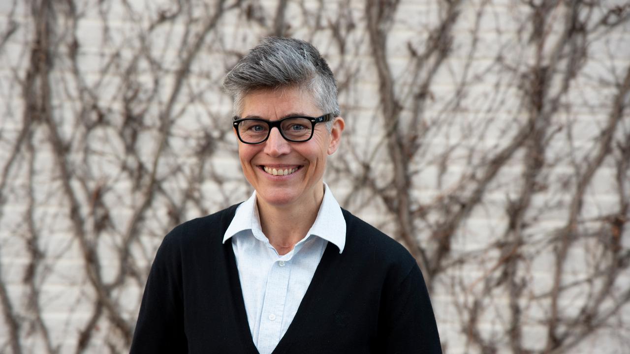 En person står framför en tegelvägg med klättrande växter på, och ler mot kameran.