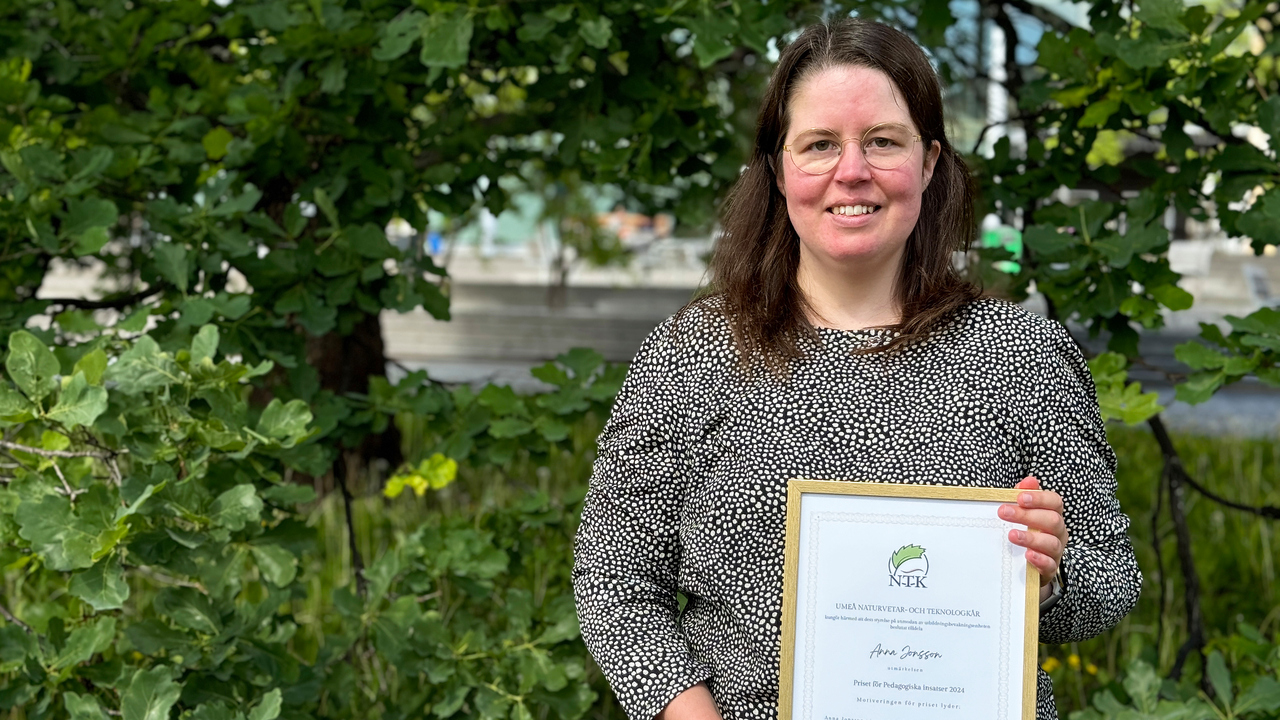 Anna Jonsson, universitetslektor i datavetenskap, har långt hår och glasögon. Hon står i en grönskande utemiljö, och håller i sitt diplom.