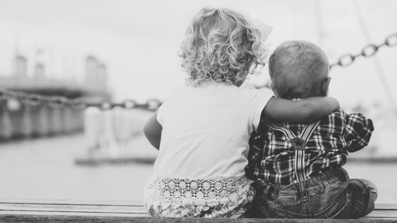 Barn som sitter ned och håller om varandra på en brygga