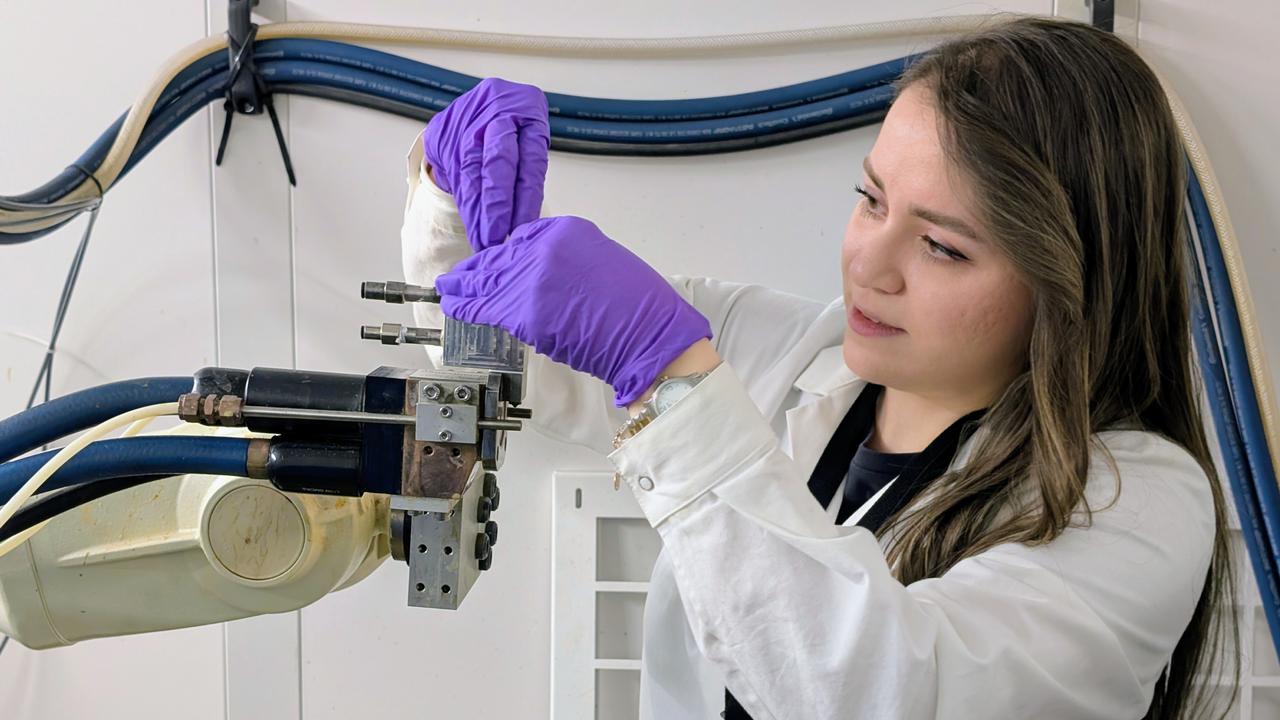 En kvinna i labbrock och handskar arbetar på en maskin.