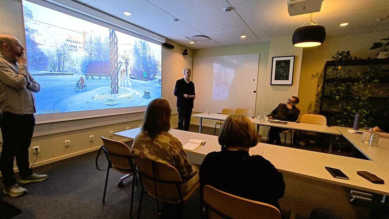 Människor sitter runt ett bord och tittar på en powerpoint.