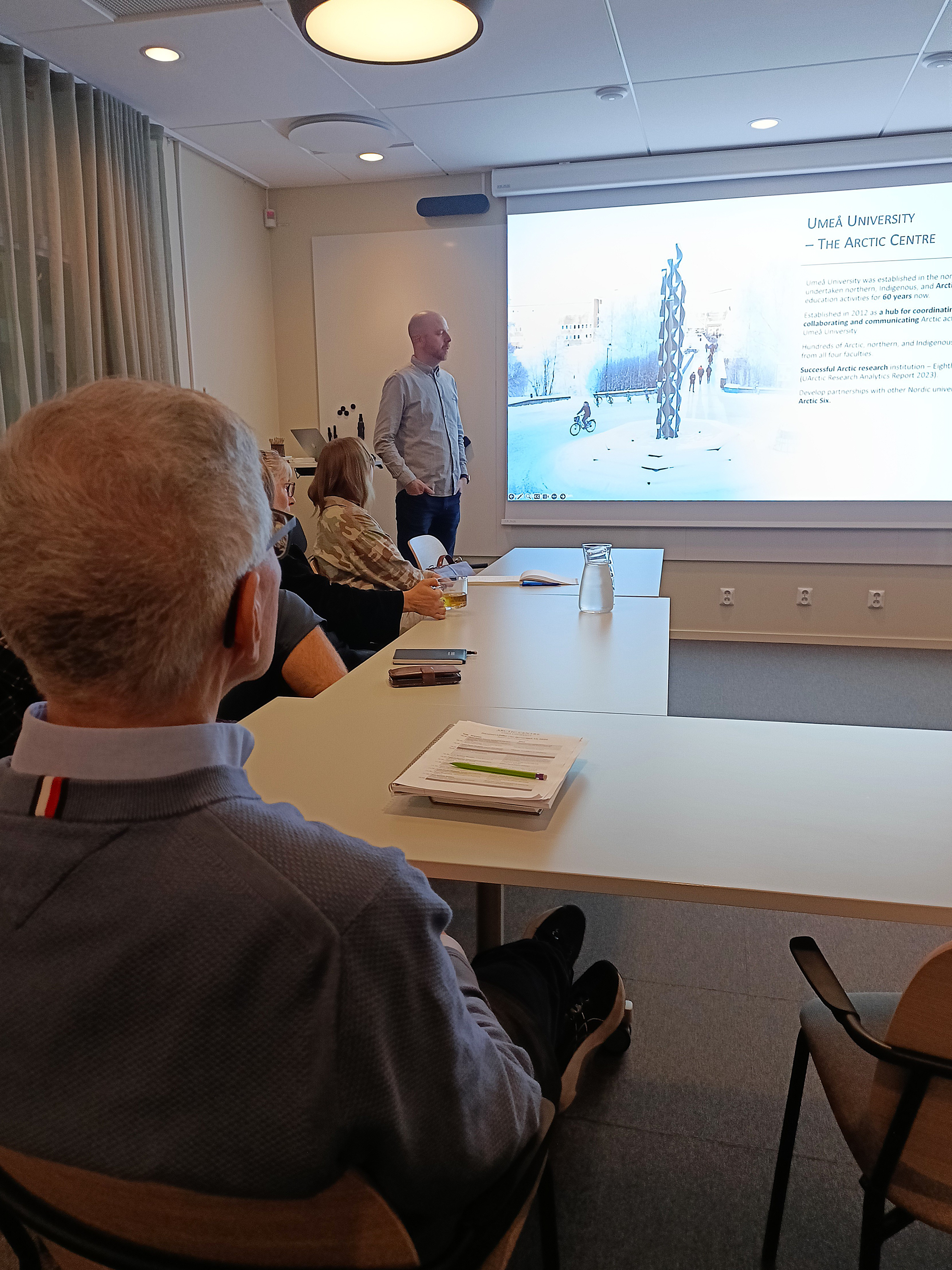 Människor sitter vid ett bord och tittar på en powerpoint.