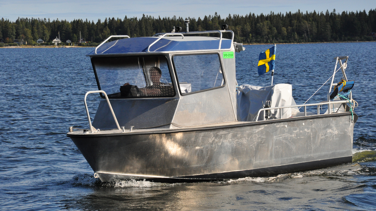 En båt av metall med stor hytt i fören och flagga i aktern
