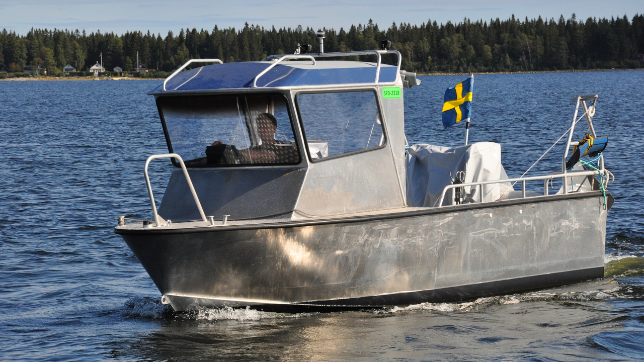 En båt av metall med stor hytt i fören och flagga i aktern