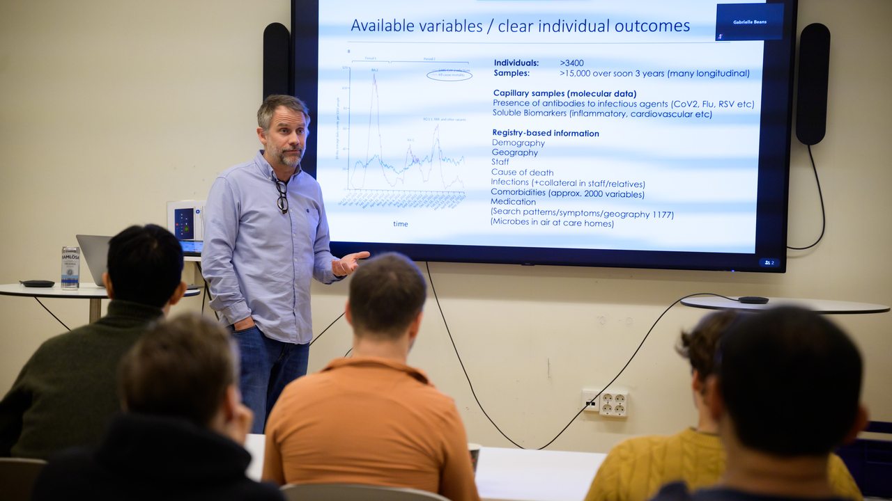 Mattias Forsell stands next a screen with a slide showing and delivers his pitch to an audience of seated researchers with their backs to the camera