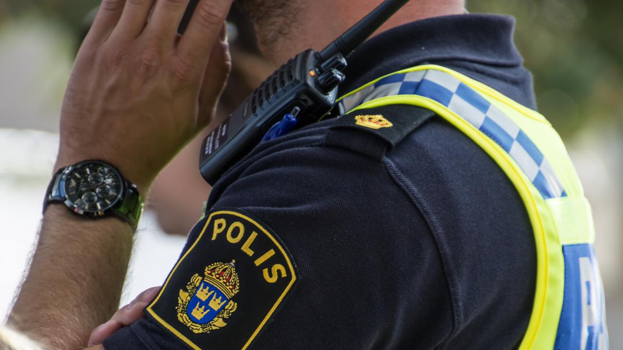 Detalj polis med uniform som pratar i mobil. Man ser arm och tröja med polisens emblem.
