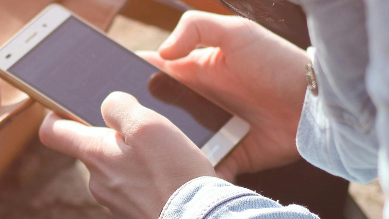 Ung person skriver på mobil. Har en brun väska framför sig.