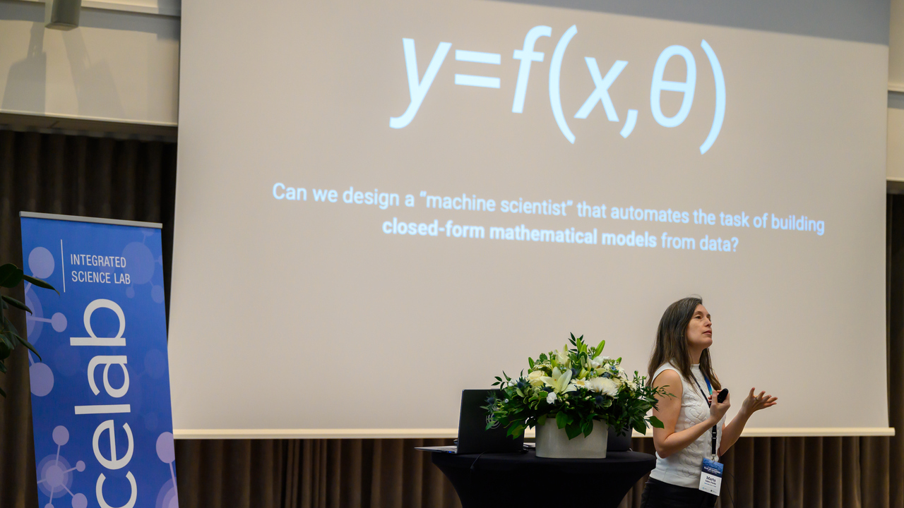 Marta Sales Pardo står framför en stor skärm, bredvid en blombukett med gröna och blå färger. Till vänster syns en banderoll där det står icelab.