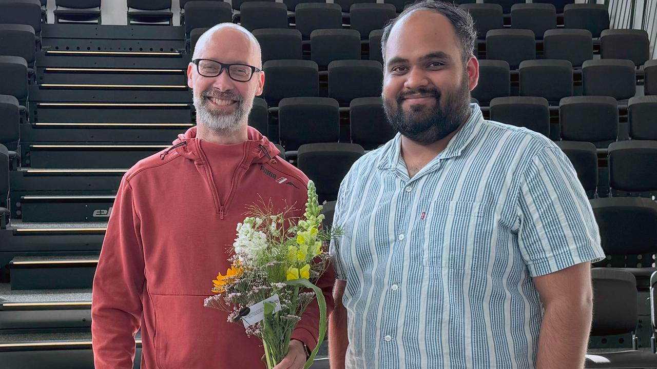 Gruppbild på Ulrik Söderstöm och Aman Malhotra framför en läktare. Ulrik håller i en blombukett.