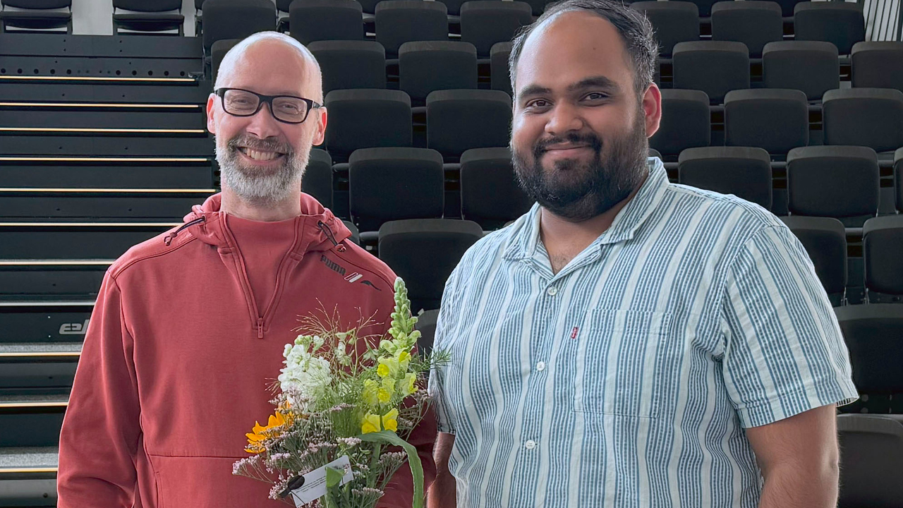 Gruppbild på Ulrik Söderstöm och Aman Malhotra framför en läktare. Ulrik håller i en blombukett.